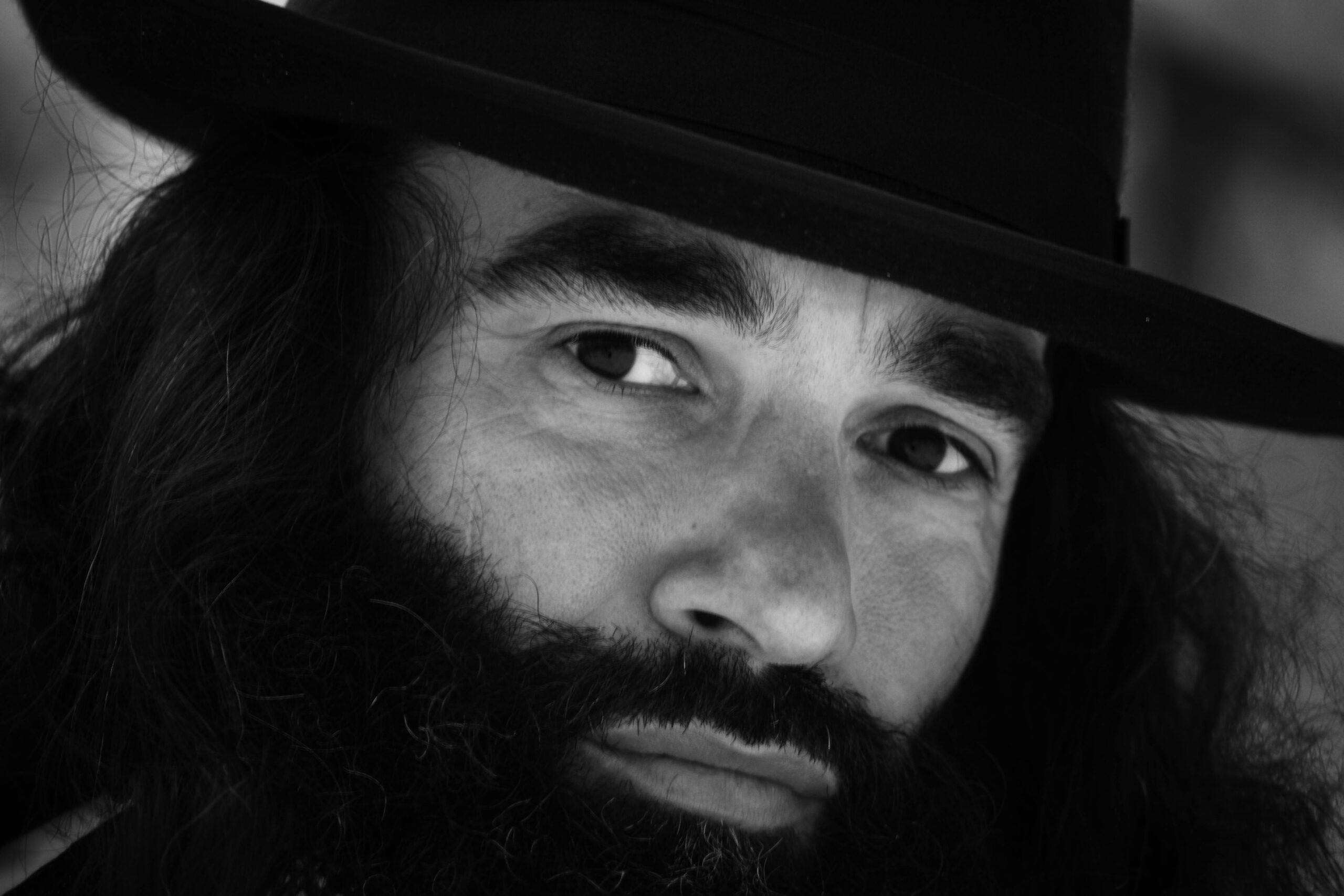 Close-up black and white portrait of a man with a beard and hat.