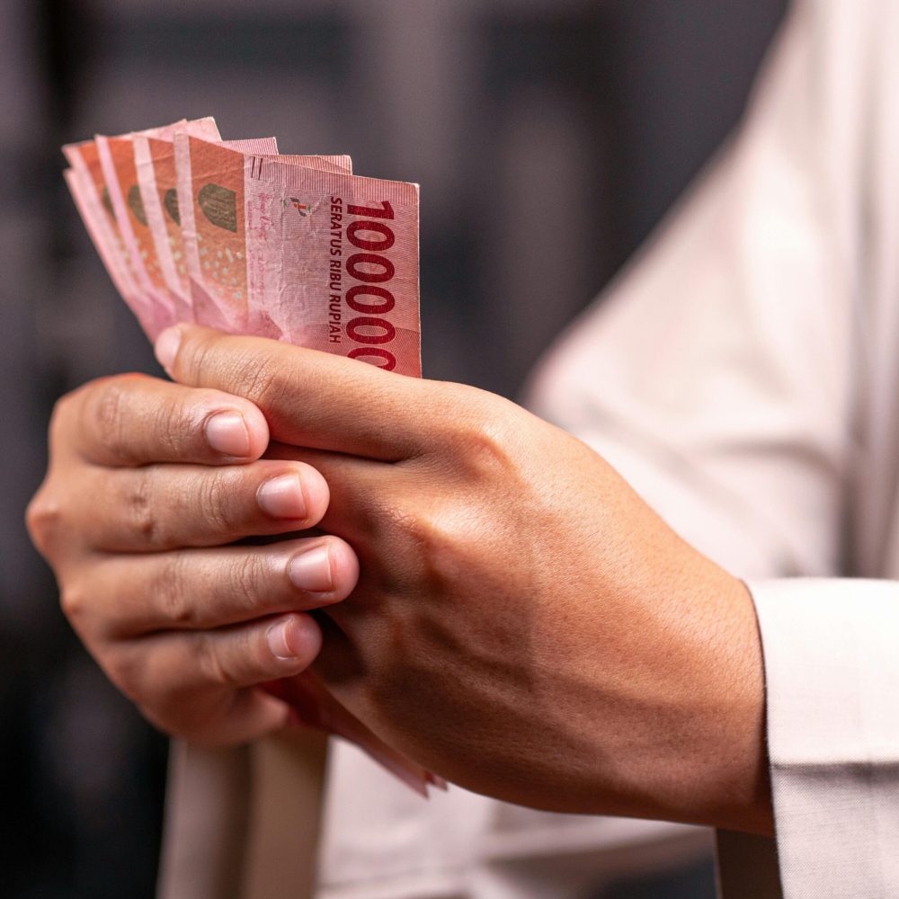 Close-up of hands holding Indonesian Rupiah 100,000 bills, highlighting financial and economic concepts.